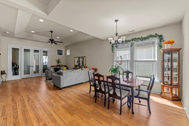 dining room featuring ceiling fan with notable chandelier, light hardwood / wood-style floors, and a raised ceiling