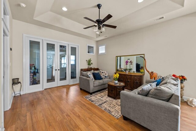 living room featuring french doors, light hardwood / wood-style flooring, ceiling fan, and a raised ceiling