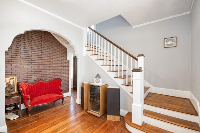 stairs with wood-type flooring, brick wall, and ornamental molding