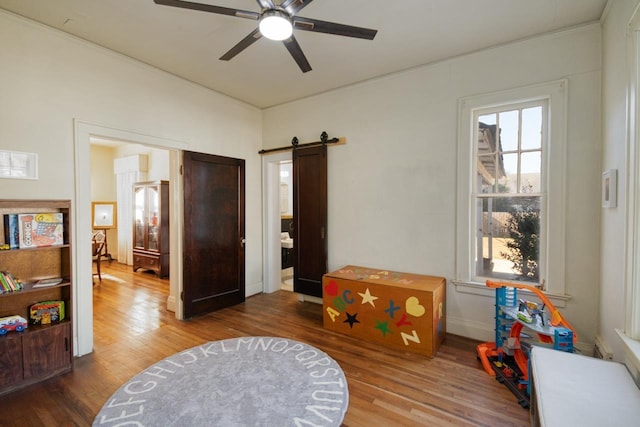 game room featuring wood-type flooring, a barn door, and ceiling fan