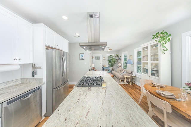 kitchen with wood finished floors, light stone countertops, stainless steel appliances, open floor plan, and island range hood