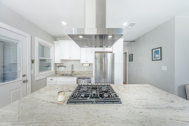 kitchen with light stone countertops, a sink, appliances with stainless steel finishes, white cabinetry, and island range hood