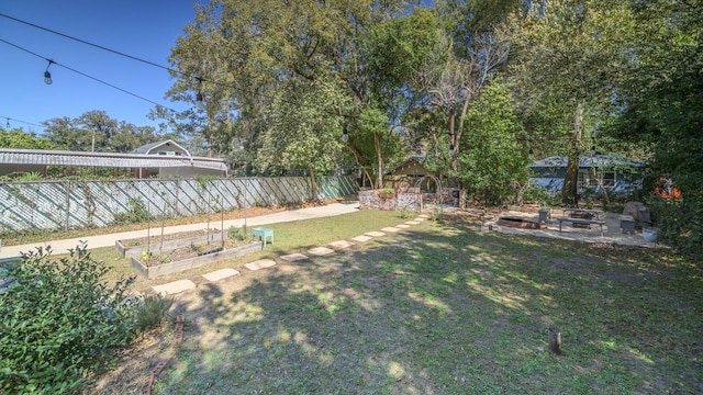 view of yard featuring a garden, a patio, fence, and an outdoor fire pit