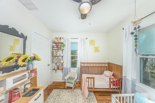 bedroom featuring dark wood finished floors, a nursery area, visible vents, and a sink