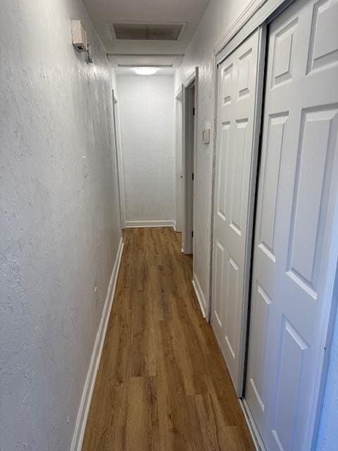 hallway featuring a textured wall, visible vents, baseboards, dark wood finished floors, and attic access