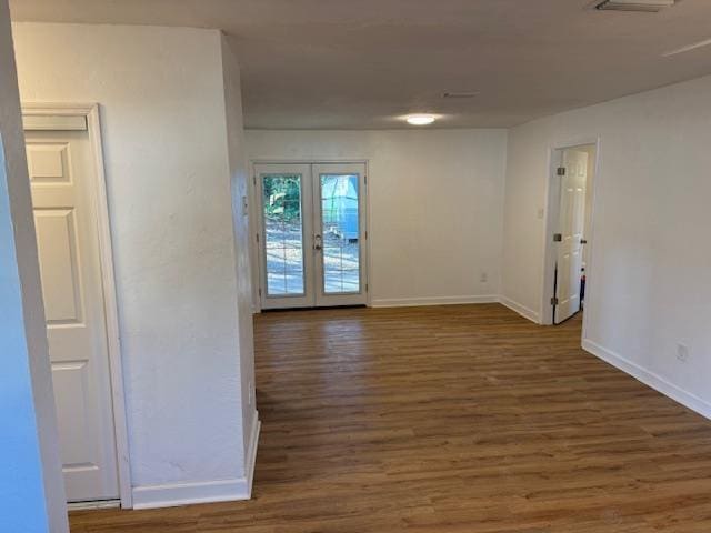 spare room featuring french doors, dark wood-type flooring, and baseboards