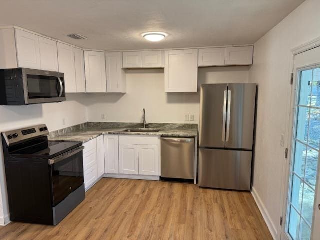 kitchen featuring dark countertops, light wood-style flooring, appliances with stainless steel finishes, white cabinetry, and a sink