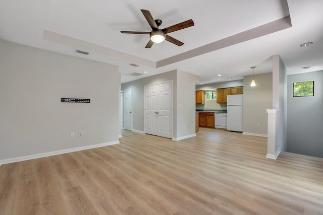 unfurnished living room featuring light wood-style floors, ceiling fan, a raised ceiling, visible vents, and plenty of natural light