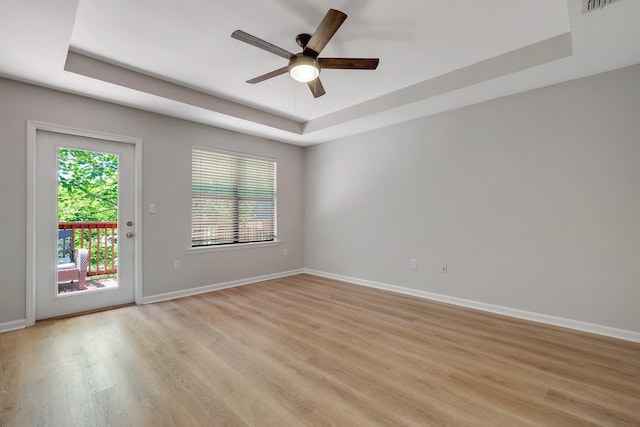 unfurnished room with a raised ceiling, ceiling fan, light wood finished floors, and baseboards