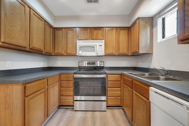 kitchen featuring a sink, visible vents, light wood-style flooring, white appliances, and dark countertops