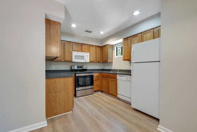 kitchen featuring light wood finished floors, a sink, white appliances, baseboards, and dark countertops