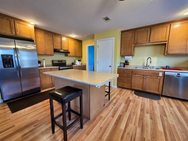 kitchen featuring sink, appliances with stainless steel finishes, a center island, light hardwood / wood-style floors, and a kitchen bar