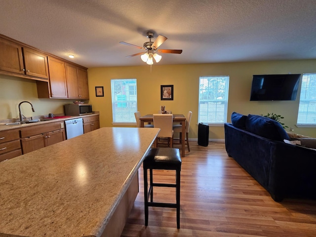 kitchen with sink, a breakfast bar area, wood-type flooring, dishwasher, and a healthy amount of sunlight