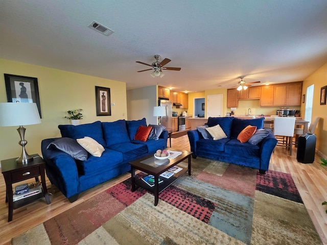 living room with a textured ceiling, light hardwood / wood-style floors, and ceiling fan