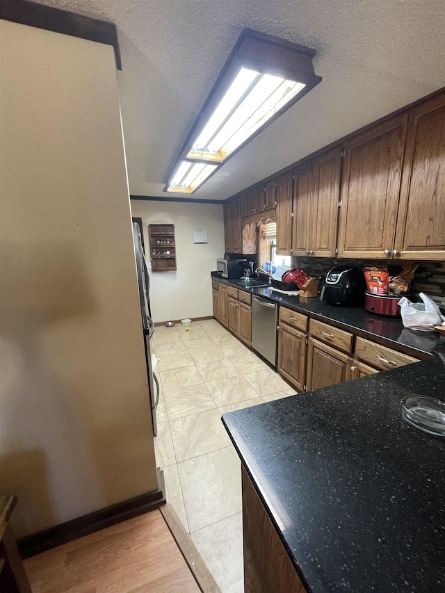 kitchen featuring dark countertops, baseboards, stainless steel appliances, light tile patterned flooring, and a textured ceiling