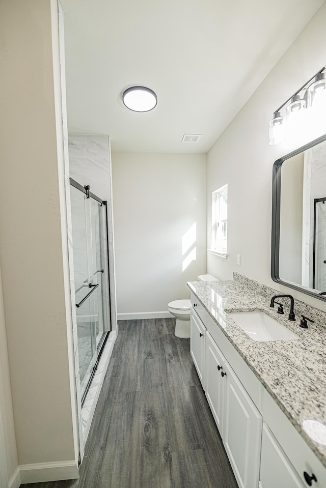 bathroom featuring toilet, wood finished floors, vanity, visible vents, and a stall shower