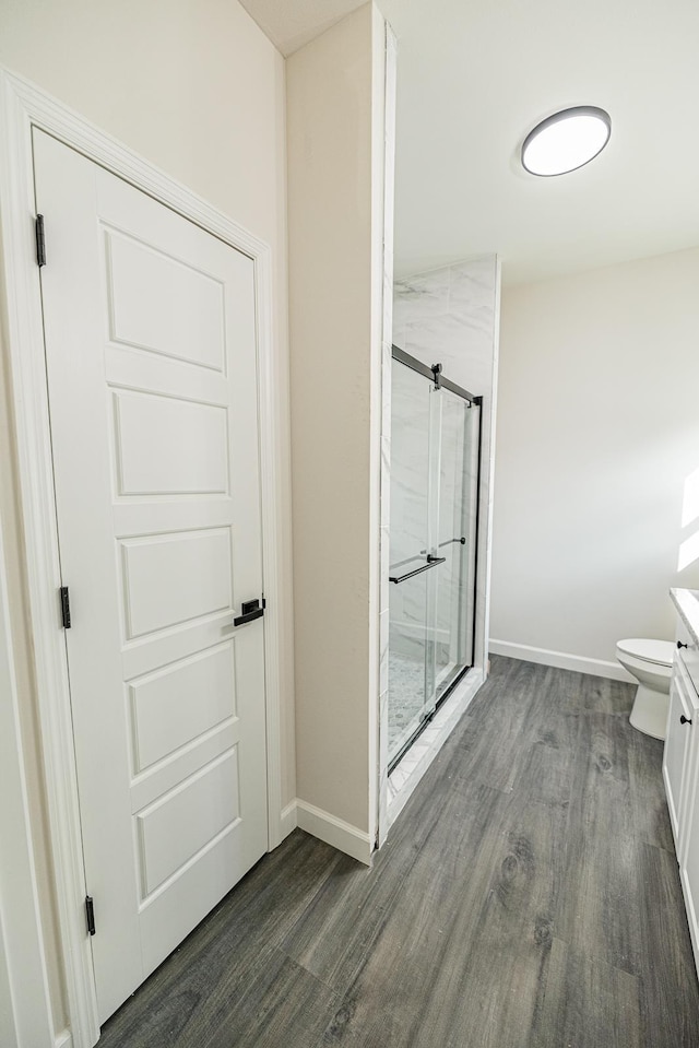 full bathroom with a stall shower, baseboards, toilet, wood finished floors, and vanity