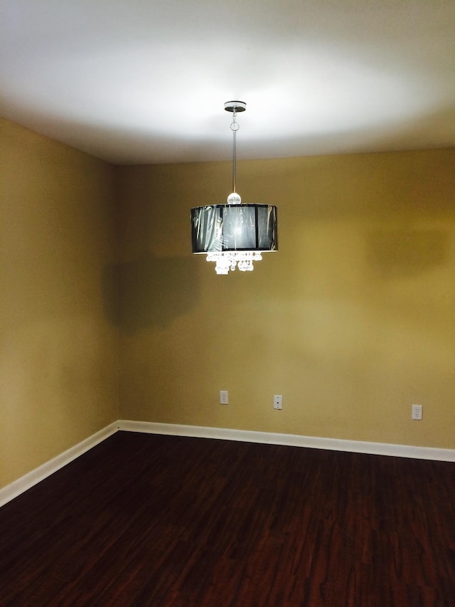 spare room featuring a notable chandelier, baseboards, and dark wood-style floors