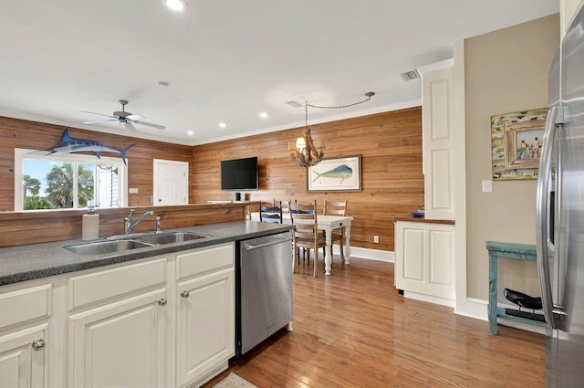 kitchen featuring stainless steel appliances, a sink, wood walls, dark countertops, and a chandelier