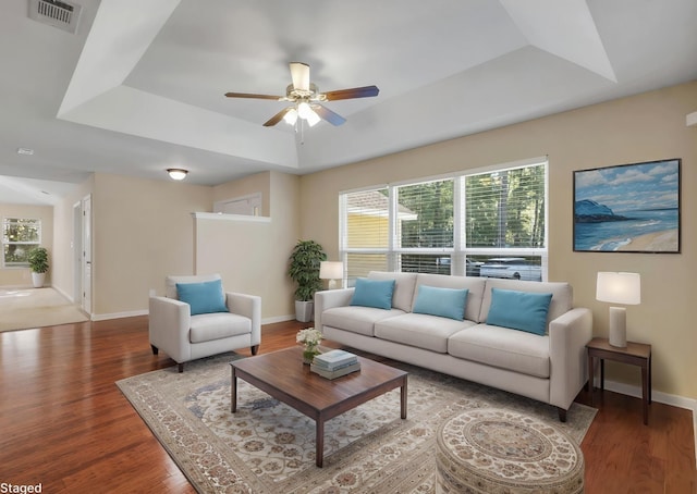 living room with a raised ceiling, a healthy amount of sunlight, visible vents, and wood finished floors