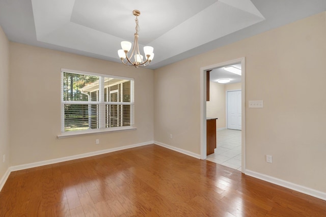 unfurnished room with a tray ceiling, wood-type flooring, baseboards, and an inviting chandelier