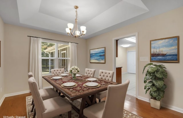 dining room with a tray ceiling, a notable chandelier, baseboards, and wood finished floors