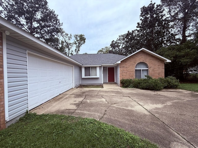 single story home featuring concrete driveway, a garage, brick siding, and roof with shingles