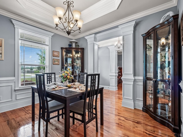 dining area featuring a chandelier, crown molding, a wainscoted wall, light wood-style flooring, and a decorative wall