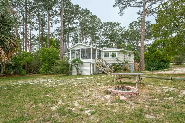 back of property featuring an outdoor fire pit, a lawn, and a sunroom