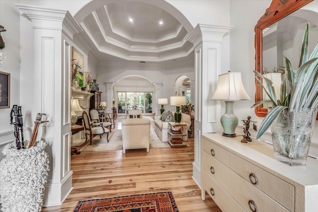 living area featuring decorative columns, a high ceiling, ornamental molding, light hardwood / wood-style floors, and a raised ceiling