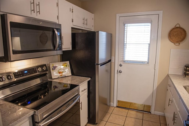 kitchen with appliances with stainless steel finishes, tasteful backsplash, white cabinetry, light tile patterned floors, and light stone counters