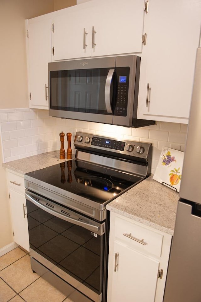 kitchen with light tile patterned flooring, white cabinets, decorative backsplash, light stone counters, and stainless steel appliances