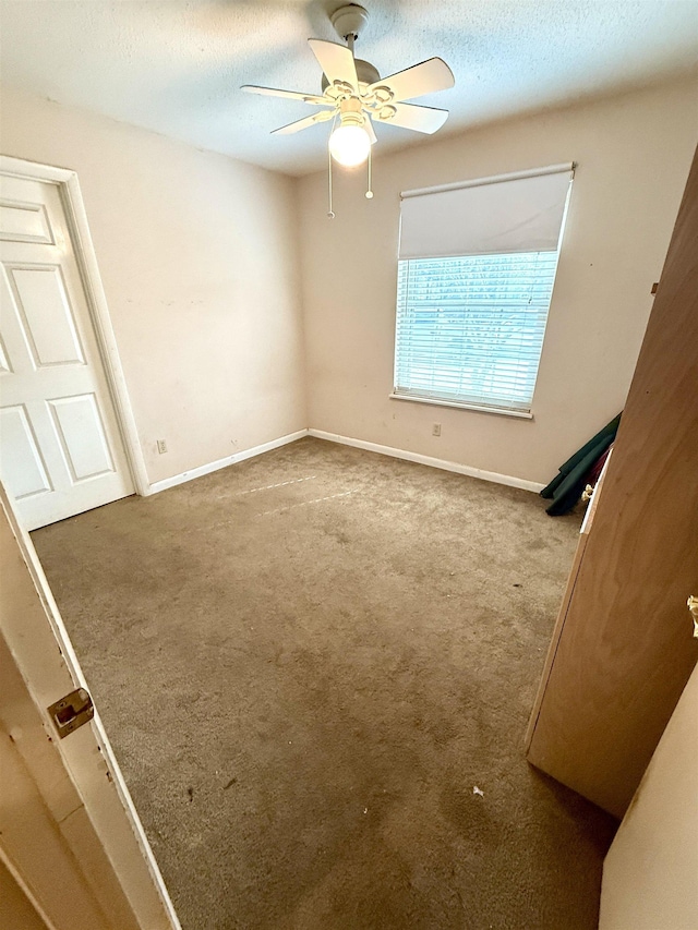 unfurnished bedroom featuring carpet floors, a textured ceiling, baseboards, and a ceiling fan