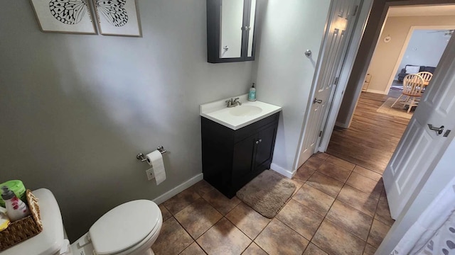 half bathroom with baseboards, toilet, vanity, and tile patterned flooring