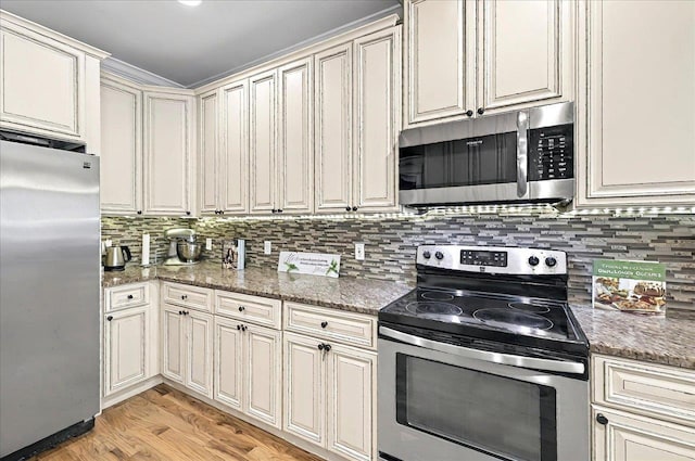 kitchen with cream cabinetry, appliances with stainless steel finishes, decorative backsplash, and light wood-style floors