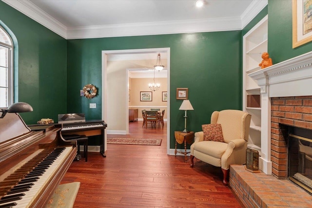 sitting room featuring ornamental molding, a fireplace, wood-type flooring, and an inviting chandelier