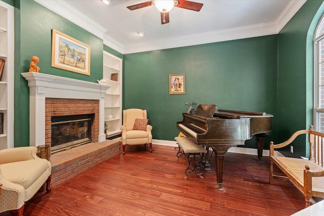 living area with built in features, ornamental molding, hardwood / wood-style floors, a brick fireplace, and ceiling fan