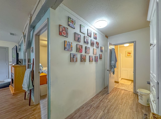 hall with light wood-type flooring and a textured ceiling