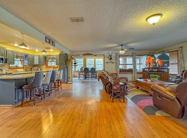 living room with light wood-type flooring, a textured ceiling, and ceiling fan