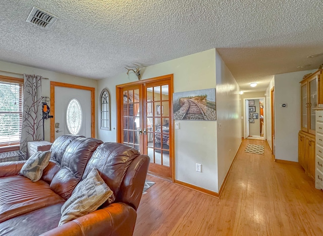 living room with light hardwood / wood-style floors, a textured ceiling, and french doors