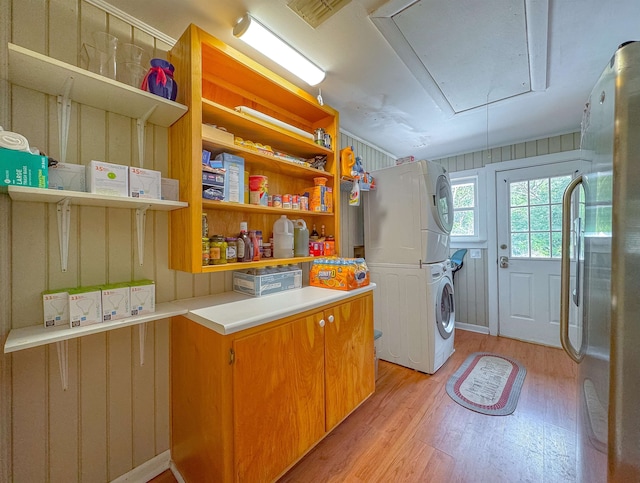 clothes washing area featuring wood walls, stacked washer and dryer, and light hardwood / wood-style flooring