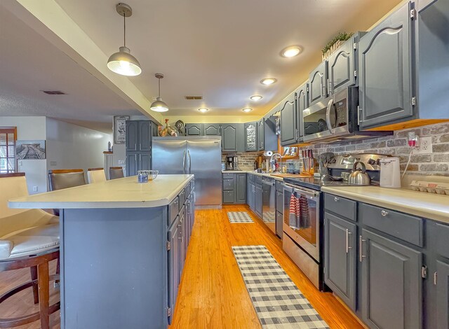 kitchen featuring stainless steel appliances, a kitchen island, decorative light fixtures, light hardwood / wood-style floors, and a kitchen breakfast bar