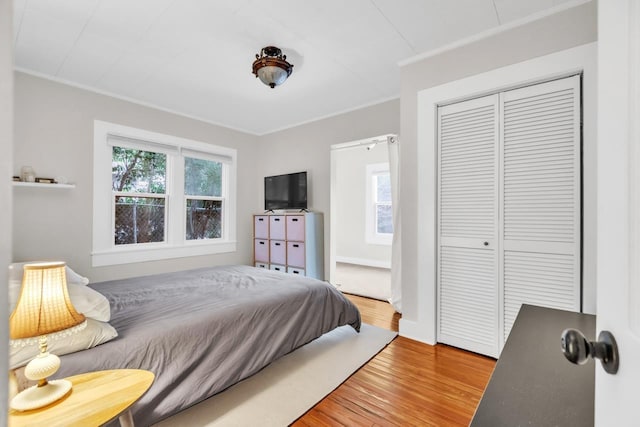 bedroom with wood-type flooring, crown molding, and a closet