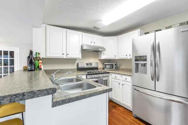 kitchen featuring a kitchen bar, sink, appliances with stainless steel finishes, kitchen peninsula, and white cabinets