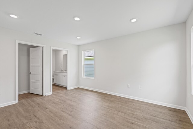 unfurnished bedroom featuring ensuite bathroom and light wood-type flooring