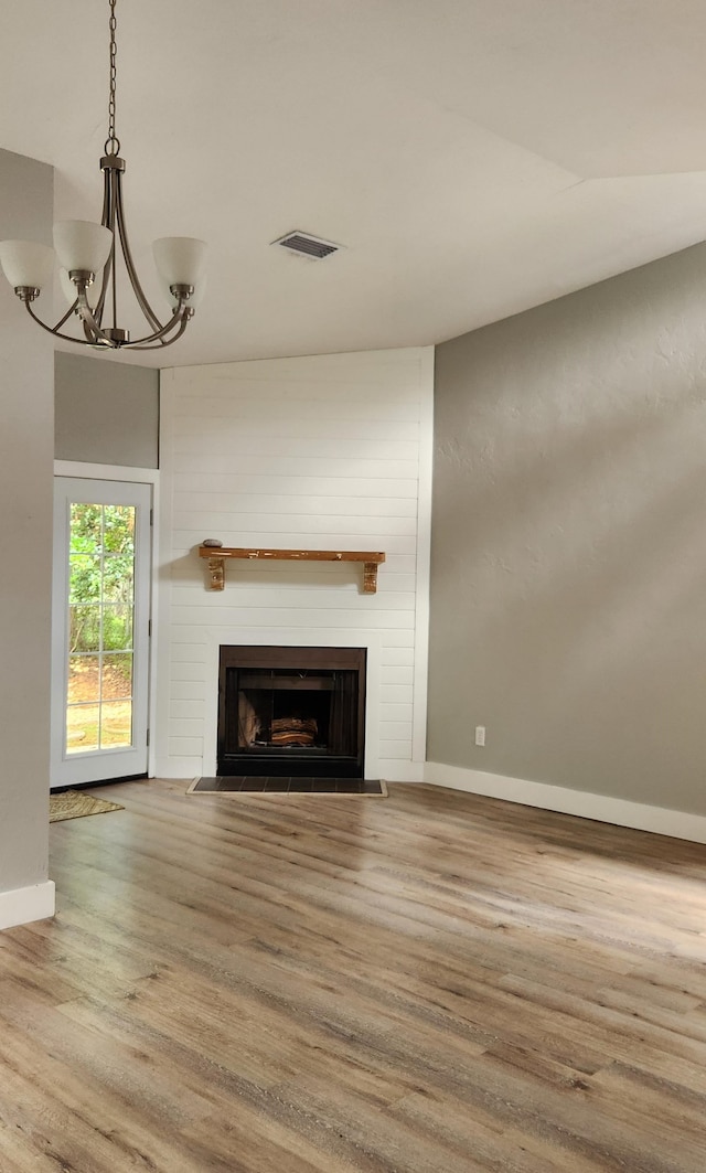 unfurnished living room featuring hardwood / wood-style flooring, an inviting chandelier, and a large fireplace