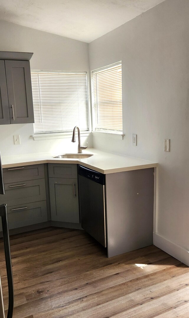 kitchen featuring stainless steel dishwasher, hardwood / wood-style flooring, gray cabinetry, and sink