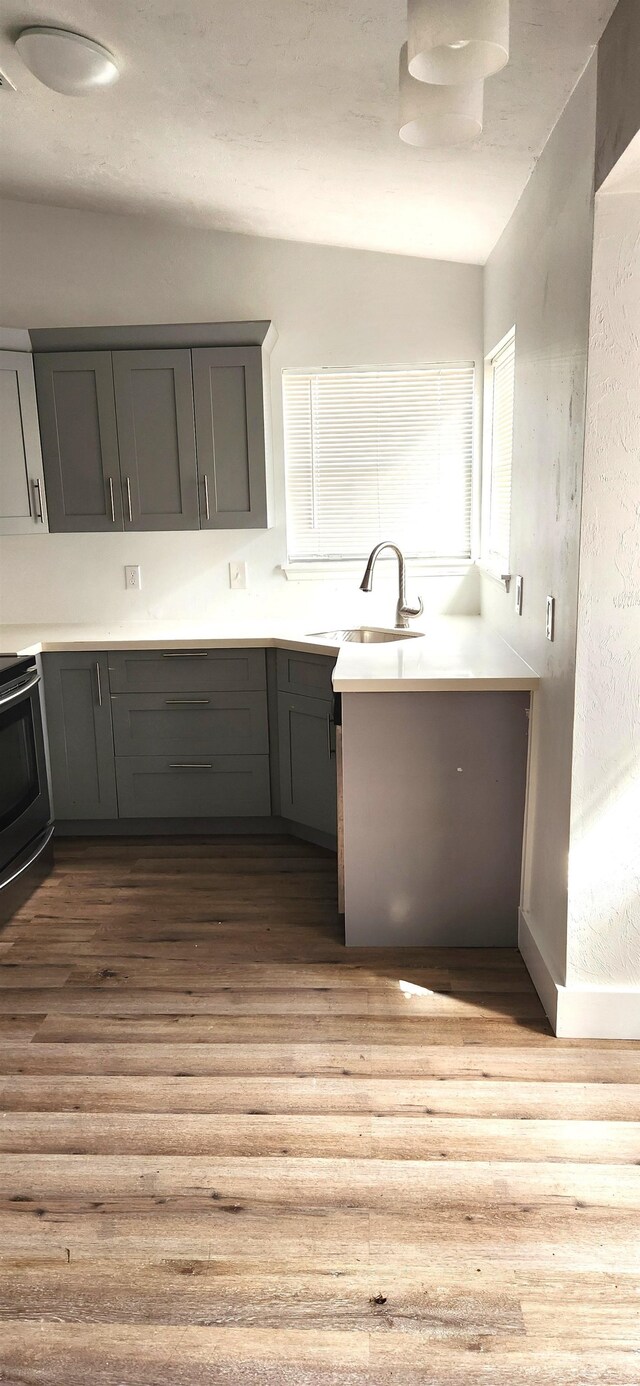 kitchen with gray cabinets, stainless steel stove, sink, and light wood-type flooring