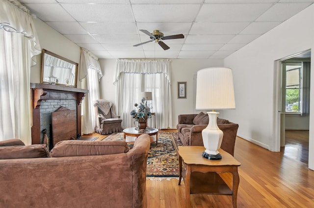 1118 W Green St, Perry, FL 32347 - living room with a ceiling fan, light wood-style floors, a paneled ceiling, a brick fireplace, and baseboards