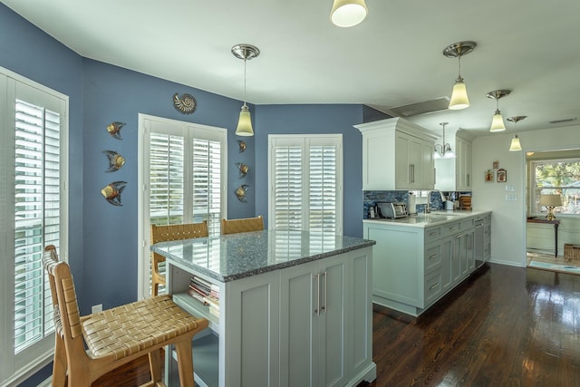 kitchen with tasteful backsplash, white cabinetry, dark hardwood / wood-style flooring, hanging light fixtures, and light stone countertops